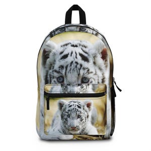 Op de afbeelding: Rugzak met een ontwerp van een witte tijgerwelp. De hoofdafbeelding toont een close-up van een witte tijgerwelp met blauwe ogen en zwarte strepen. Een kleinere afbeelding van een welp staat op de voorzak. Zwarte handgreep en zwarte rits.