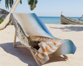 May include: A beach chair with a colorful beach towel featuring a nautilus shell design. The towel has shades of blue, white, and brown. The chair is on a sandy beach with palm trees and a boat in the background.