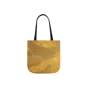 Op de afbeelding: Een tote bag met een ontwerp van gouden munten die uit zwarte ketels stromen. De tas heeft een geel en goud kleurenschema met zwarte handvatten, perfect voor het dragen van boeken of boodschappen.