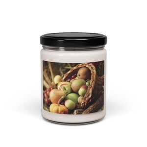 Puede incluir: Un tarro de vidrio para velas con tapa negra y una etiqueta que muestra una cornucopia llena de una variedad de frutas y verduras, incluyendo manzanas, peras, uvas y una pequeña calabaza.