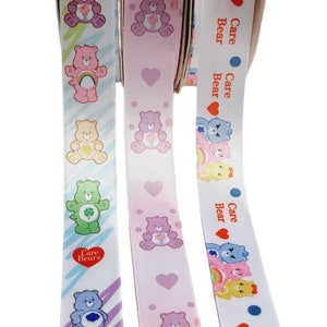 K&ouml;nnte beinhalten: Drei Rollen Band mit Care Bears-Designs. Die B&auml;nder zeigen verschiedene Care Bears-Charaktere, Herzen und Regenbogen. Die B&auml;nder sind in Pastellfarben gehalten, darunter Rosa, Blau, Gelb und Gr&uuml;n. Der Text "Care Bears" ist auf den B&auml;ndern aufgedruckt.