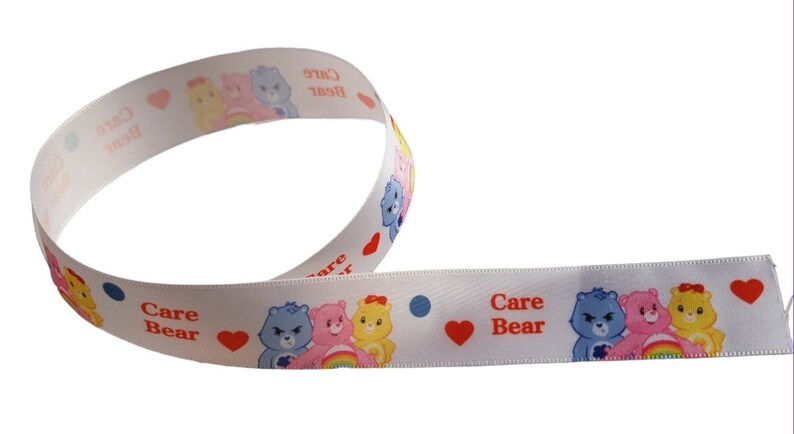 K&ouml;nnte beinhalten: Wei&szlig;es Band mit Care Bears-Figuren, Herzen und Punkten. Das Band zeigt die Worte "Care Bear" in Rot. Das Band ist gewellt und eignet sich f&uuml;r Bastelarbeiten oder zum Verpacken von Geschenken.