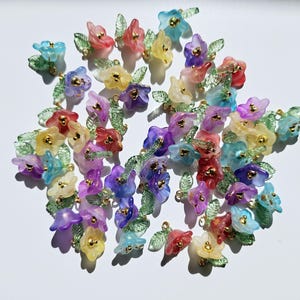May include: A collection of colourful, translucent flower charms in shades of blue, red, yellow, purple, and green. Each charm features a small gold-coloured centre and delicate green leaves. These charms are ideal for jewellery making or craft projects.