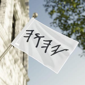 May include: A white flag with black Hebrew script waving in the wind. The flag is mounted on a silver pole with a gold finial. The background includes a building and a tree.