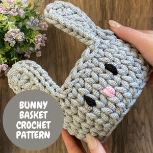 May include: A crocheted grey bunny basket with black eyes and a pink nose. The basket has long ears and is held by a person. The text "BUNNY BASKET CROCHET PATTERN" is in a grey circle.