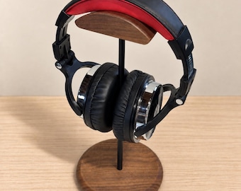 May include: Black and red OneOdio over-ear headphones resting on a wooden stand. The headphones feature a black headband with a red inner cushion, black ear cups with silver accents, and the brand name OneOdio printed on the top headband.