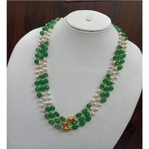 May include: A three-strand necklace with green and white beads. The necklace has a gold clasp in the center.