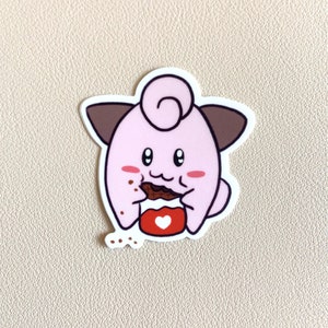 May include: A pink cartoon character with brown ears and a curled tail is eating a chocolate bar. The character is holding the chocolate bar in its front paws and has a red heart on its chest.