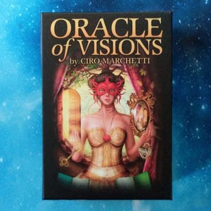 May include: A tarot card box with the title "ORACLE of VISIONS" by Ciro Marchetti. The artwork features a woman in a red mask and gold corset, holding a mirror and key. The background is a fantasy scene with a door and curtains.