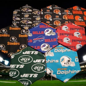 May include: A collection of hexagon-shaped fabric pieces, each featuring a different NFL team logo and colors. Teams include the Ravens, Bengals, Browns, Steelers, Bills, Patriots, Jets, and Dolphins. The background shows a football field.