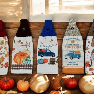 May include: Five kitchen towels with fall-themed designs. The towels feature images of pumpkins, a truck, leaves, and gnomes. The text on the towels includes "Grateful", "Thankful", "Hello Fall", "Farm Fresh Pumpkins", and "Gnome Sweet Gnome".