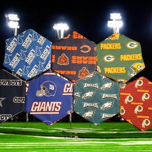 May include: A collection of seven hexagonal fabric pieces, each featuring a different NFL team logo and colors. Teams include the Lions, Bears, Packers, Cowboys, Giants, Eagles, and Redskins. The background shows a football field.