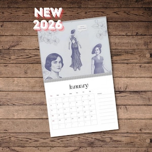 Puede incluir: Calendario de 2026 con ilustraciones de mujeres con vestidos vintage. La página de enero es visible, con una vista mensual. Las palabras "NEW 2026" están en rojo. El calendario está sobre una superficie de madera.