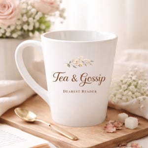 May include: A white ceramic mug with the words "Tea & Gossip" and "Dearest Reader" printed in brown script. The mug has a floral design and a gold spoon rests on a wooden board.