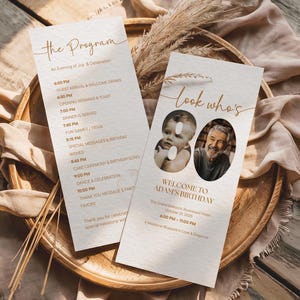 May include: Two cream-coloured birthday program cards with gold text and photos. One card reads "The Program" with a schedule. The other says "Look who's 80" with photos and event details. The cards are on a wooden tray.