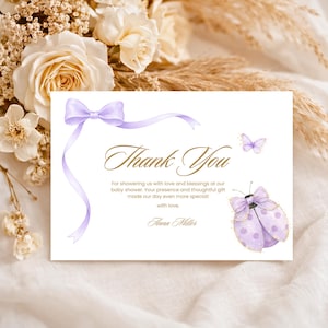 May include: A baby shower thank you card with a lavender bow and ribbon design. The card features a butterfly and ladybug illustration, with the words "Thank You" in elegant script. The card includes a personalized message.