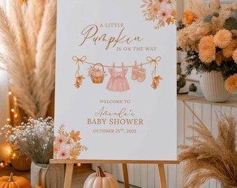 May include: A white sign on an easel with the text "A Little Pumpkin is on the Way" and "Welcome to Aanda's Baby Shower October 25th, 2025". The sign has floral and baby-themed illustrations. Pumpkins and floral arrangements surround the sign.
