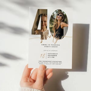 Może przedstawiać: Białe zaproszenie z wyciętą liczbą 40, z dwoma zdjęciami. Tekst brzmi "Emma wkrótce kończy czterdzieści lat!" ze szczegółami wydarzenia. Karta jest trzymana przez osobę.