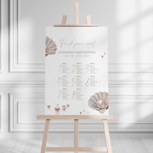 Puede incluir: Un plano de asientos blanco con una fuente de escritura rosa que dice "Find your seat. Stephanie's Baby Shower. January 22nd, 2023". El gráfico está decorado con ilustraciones de perlas y una concha grande.