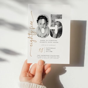 Peut inclure: Une carte d'invitation blanche avec des lettres dorées annonçant une fête d'anniversaire pour Sara qui fête ses quatre-vingt-cinq ans. L'invitation comprend une photo en noir et blanc de Sara et d'une version plus jeune d'elle-même. Le texte indique "Sara a quatre-vingt-cinq ans. Rejoignez-nous pour célébrer ! Samedi, avril 18 à 14h00. Le jardin des Thompson, 23 Oak Street, Springfield, USA. RSVP à Sara au 323-456789."
