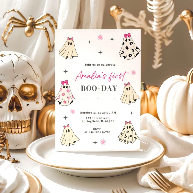 May include: A Halloween-themed invitation with the text "Amalia's first BOO-DAY" and ghost illustrations. The invitation is on a white plate with gold trim, surrounded by Halloween decorations, including a skull, spider, and pumpkins.