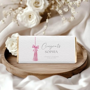 Op de afbeelding: Een witte chocolade reep met een roze kwast en strik ontwerp. De tekst op de reep luidt "Congrats Sophia University of Melbourne Class of 2023".