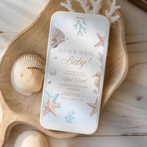 Puede incluir: Un smartphone muestra una invitación a un baby shower con un diseño de temática marina. La invitación dice "Sea You Soon, Baby!" y presenta ilustraciones de conchas marinas, estrellas de mar e hipocampos. El teléfono descansa sobre una bandeja de madera con conchas.