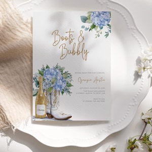 Puede incluir: Invitación a una despedida de soltera con las palabras "Boots & Bubbly" en escritura dorada. La invitación presenta una ilustración de acuarela de una botella de champán, botas de vaquero blancas e hortensias azules. La invitación está sobre un fondo blanco.