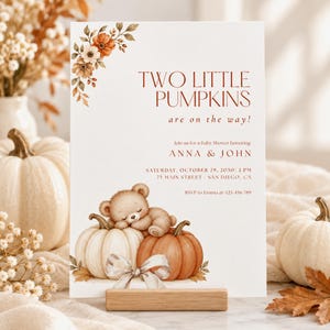 Puede incluir: Una tarjeta de invitación rectangular blanca para un baby shower con el texto TWO LITTLE PUMPKINS are on the way! y detalles para Anna y John. El diseño incluye ilustraciones en acuarela de un osito de peluche durmiendo sobre dos calabazas.