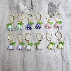 May include: Ten pairs of gold earrings with delicate flower charms. The charms are in various colors, including white, purple, pink, and green.
