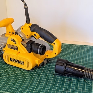 May include: A yellow and black DeWalt belt sander with a dust collection hose attached. The sander has a black handle and a silver base. The hose is connected to the sander with a black adapter.