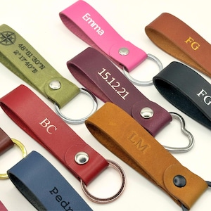 Puede incluir: Una colección de llaveros de cuero de diferentes colores y grabados. Los llaveros presentan una variedad de grabados, incluyendo nombres, iniciales, fechas y coordenadas. Los llaveros están todos unidos a llaveros de plata.