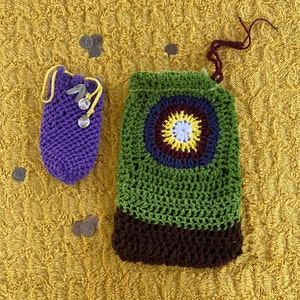 May include: Two crocheted bags, one purple and one green with a brown bottom. The green bag has a colorful circular design in the center.