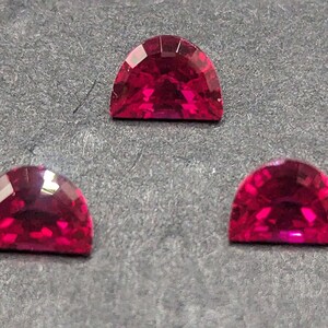 May include: Three red gemstone cabochons in a half-moon shape. The gemstones are set on a gray background.