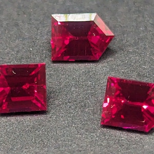 May include: Three red gemstone cabochons with a faceted cut. The gemstones are set in a square shape with a pointed top and bottom.