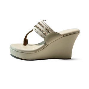 May include: A pair of off-white wedge sandals with a decorative gold chain detail on the strap.