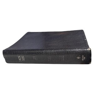 May include: A side view of a black leather-bound Holy Bible. The spine is labelled "Holy Bible" and "King James Version." The book shows signs of wear, with legible text and a cross symbol. The publisher is Nelson 495.
