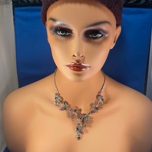 May include: A silver necklace with a delicate, leafy design. The necklace is adorned with pink, green, and black gemstones.