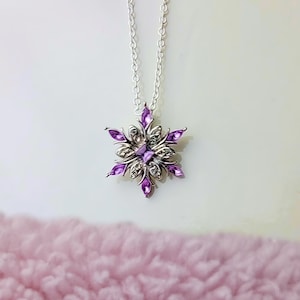 May include: A silver chain necklace with a purple snowflake pendant. The snowflake is made of silver and has purple crystals.