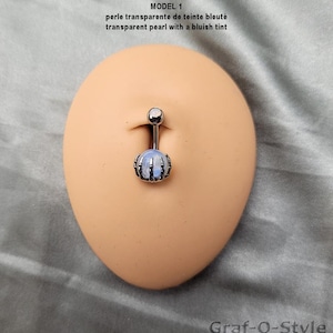May include: A silver belly button ring with a transparent, bluish pearl. The ring features a decorative design around the pearl and a small ball at the top. The text "MODEL 1" and "Graf-O-Style" are visible.