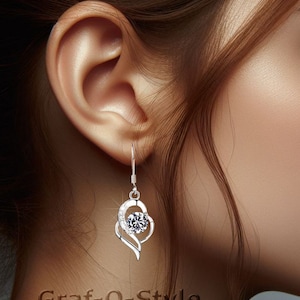 May include: Silver dangle earrings with a clear crystal in the centre of a heart-shaped design.