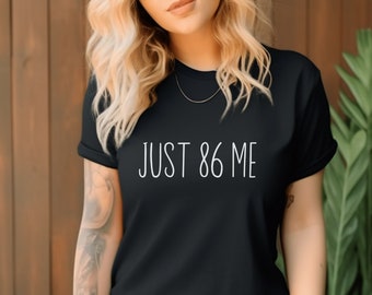Może przedstawiać: Czarny T-shirt z białym napisem "JUST 86 ME".