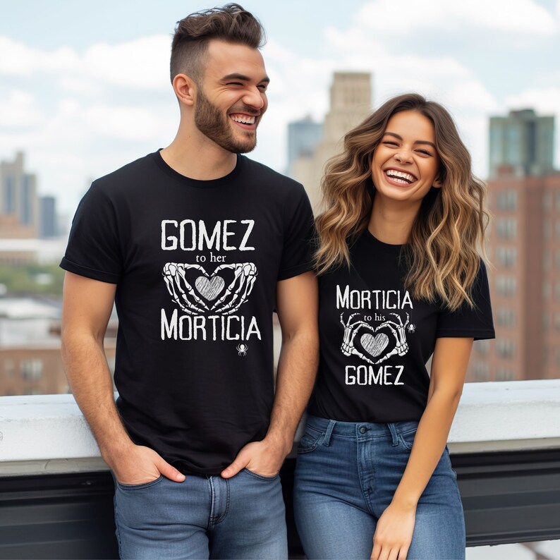 May include: Black t-shirts with white text. One shirt says "GOMEZ to her MORTICIA" with a heart and skeleton hands graphic. The other shirt says "MORTICIA to his GOMEZ" with a similar design. A small spider graphic is below the text.
