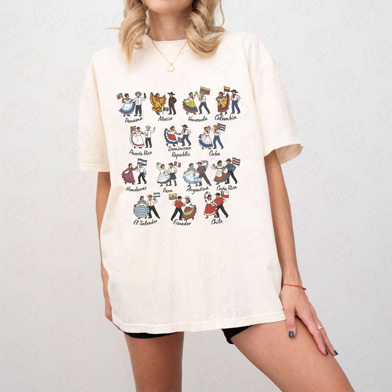 Puede incluir: Camiseta color crema con una colorida ilustraci&oacute;n de parejas bailando con trajes tradicionales, cada una representando un pa&iacute;s latinoamericano. Los nombres de los pa&iacute;ses est&aacute;n impresos debajo. Estilo casual y c&oacute;modo.