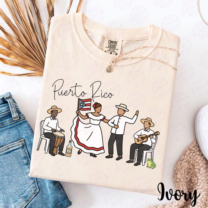 Pu&ograve; includere: T-shirt color avorio con una grafica di persone portoricane in abiti tradizionali, con la scritta "Puerto Rico" in corsivo. Il disegno include una bandiera, musicisti e una bottiglia. Una delicata collana &egrave; drappeggiata sulla maglietta.