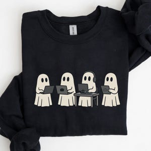 May include: Black sweatshirt featuring a graphic of four cartoon ghosts. Three ghosts are using laptops, and one is using a desktop computer with headphones. The ghosts are in a light beige color with black eyes.