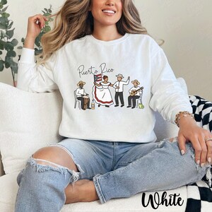 Pu&ograve; includere: Felpa bianca a maniche lunghe con una grafica raffigurante persone portoricane in abiti tradizionali. Le parole "Puerto Rico" sono sopra la grafica. La parola "White" &egrave; stampata in basso.