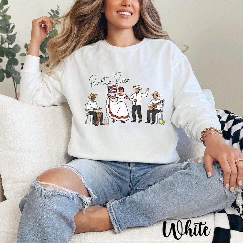 Pu&ograve; includere: Felpa bianca a maniche lunghe con una grafica raffigurante persone portoricane in abiti tradizionali. Le parole "Puerto Rico" sono sopra la grafica. La parola "White" &egrave; stampata in basso.