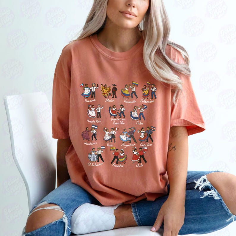 Puede incluir: Una camiseta de color coral con un gr&aacute;fico de figuras bailando que representan varios pa&iacute;ses latinoamericanos. Cada figura viste trajes tradicionales y sostiene una bandera. Los pa&iacute;ses est&aacute;n etiquetados con una fuente estilizada.