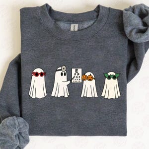 May include: Dark gray sweatshirt featuring four cartoon ghosts with sunglasses. One ghost holds a pointer to an eye chart. The other ghosts wear sunglasses with a bat, pumpkin, and red frames. The sweatshirt is a Gildan brand.